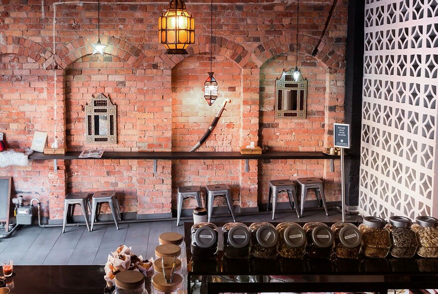 Restaurant interior with brick walls, stools at a bench and pendant Moroccan light.
