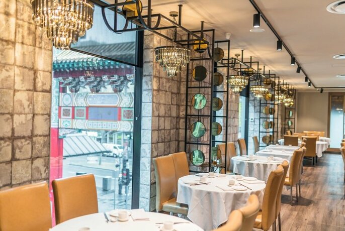 Interior of Crystal Jade restaurant, with tables set with napery and cutlery, chandeliers and view of Chinatown gateway.