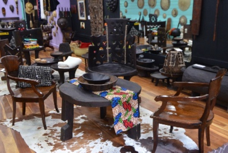 Showroom of wooden furniture and other artefacts, including colourful rugs and metal work.