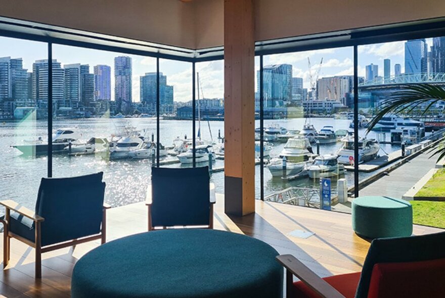 Armchairs facing a glass windowed corner of Library at The Dock, with views of Melbourne city skyline over the water. 