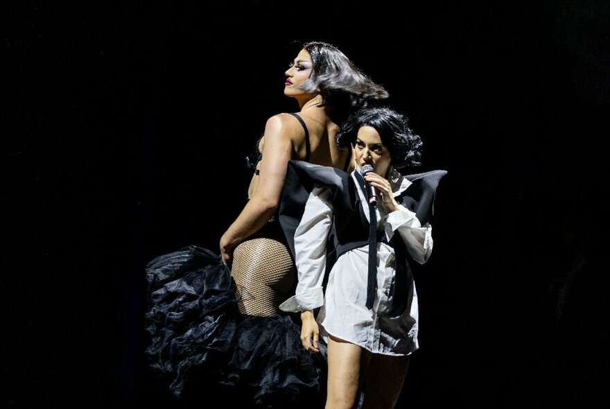 A female singer and a male drag performer on stage in black and white costumes.