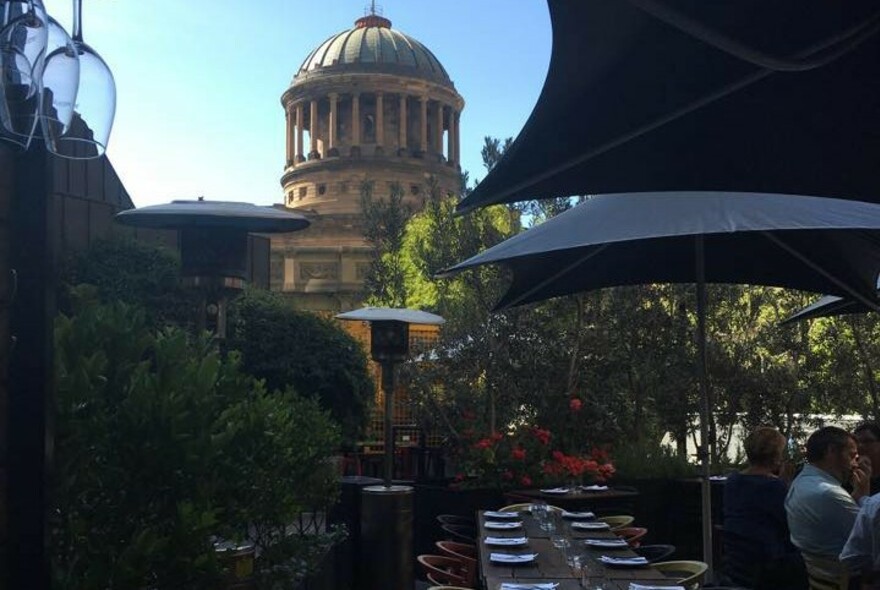 Outdoor dining area with set tables, black umbrellas and Law Courts cupola in the background.