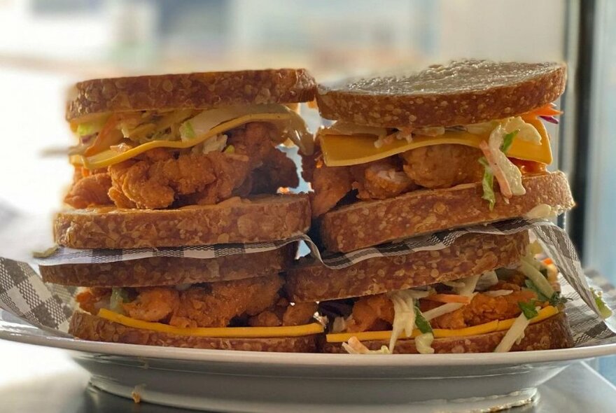 Stack of four fried chicken toasted sandwiches on a plate.