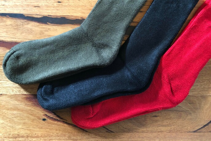 A green, navy and red sock in a row on a wooden background.
