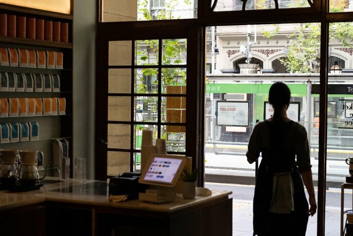 Interior of a cafe looking out onto a city street with a tram going past, and a person in silhouette in front of the window.