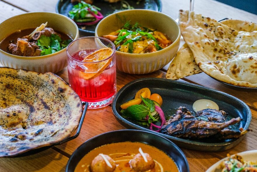 Several Indian dishes and a cocktail on a table