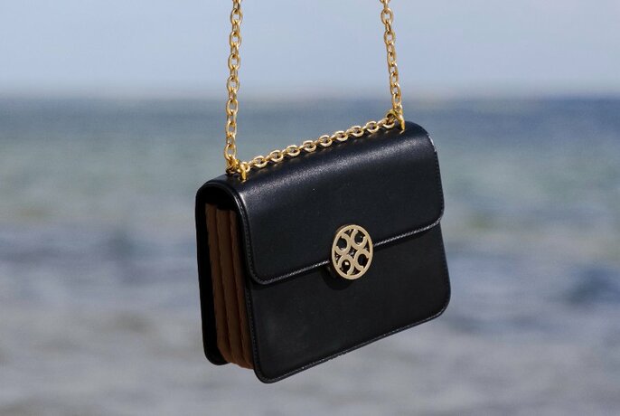 Back handbag with gold link hanging, outdoors.