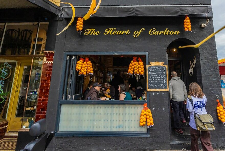 two people are walking into a small restaurant there is a sign saying Heart of Carlton
