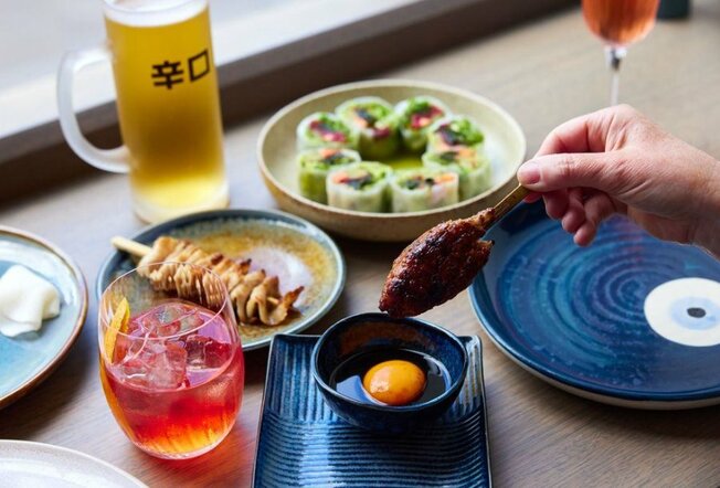 A cocktail, a beer and plates of sushi on a table.