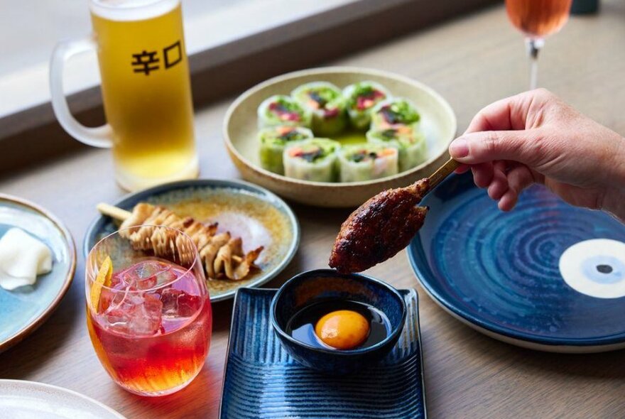 A cocktail, a beer and plates of sushi on a table.
