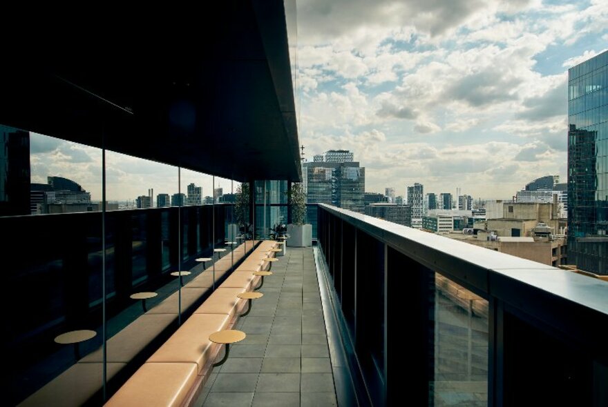 The balcony at The Q, with seats along the wall, small tables, and views of the Melbourne city skyline.
