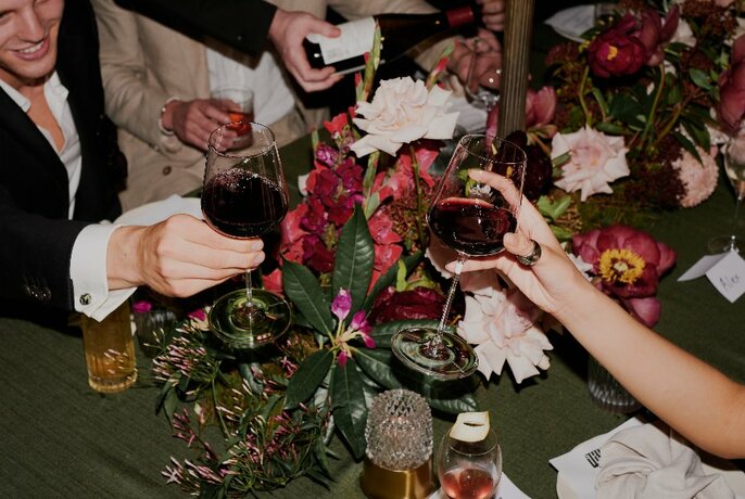 Hands clinking glasses over a table and vase of flowers.