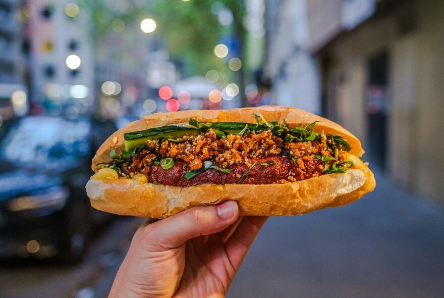 Someone holding up a sausage banh mi in the street.