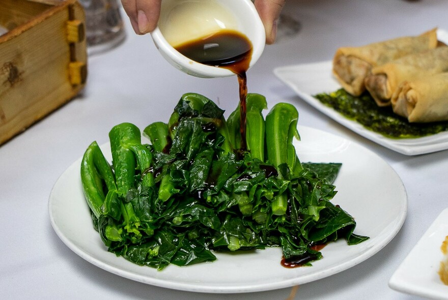 Sauce being poured over a plate of cooked bok choi.