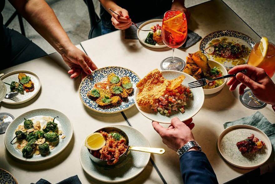 Hands reaching over a table to serve up food from a selection of share plates.