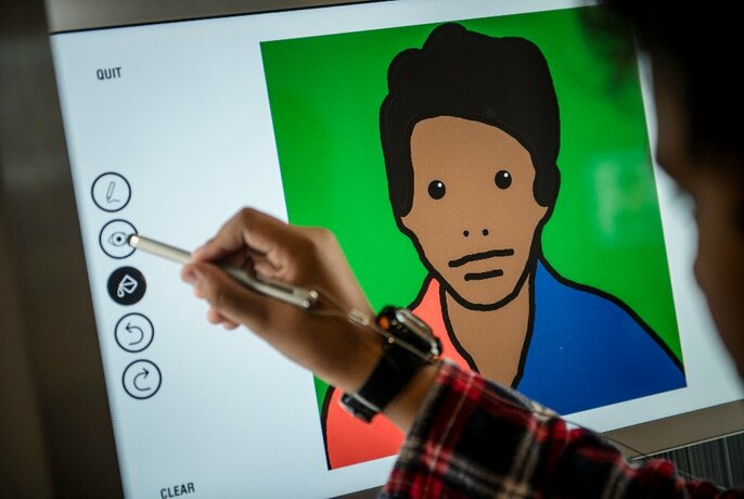 A person's hand using a digital pen to draw a portrait of themselves on a screen.