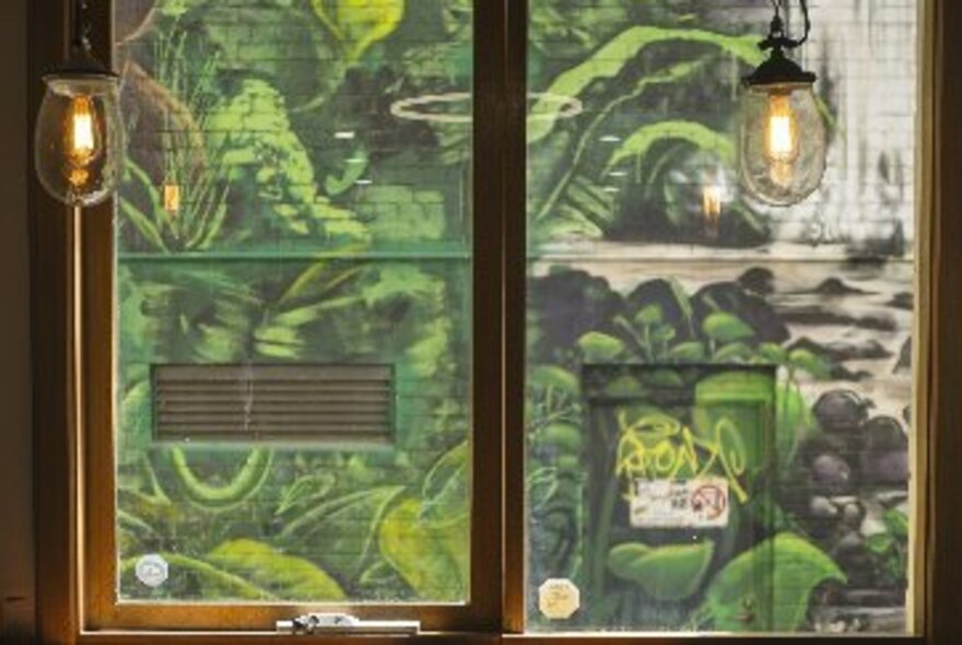 The interior window of a cafe with pendant lights and green graffiti outside 