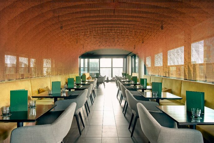 Long shot of interior of a room with banquette seating against the walls, tables and upholstered chairs.
