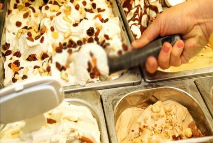 A hand scooping ice cream from a display of several flavours.