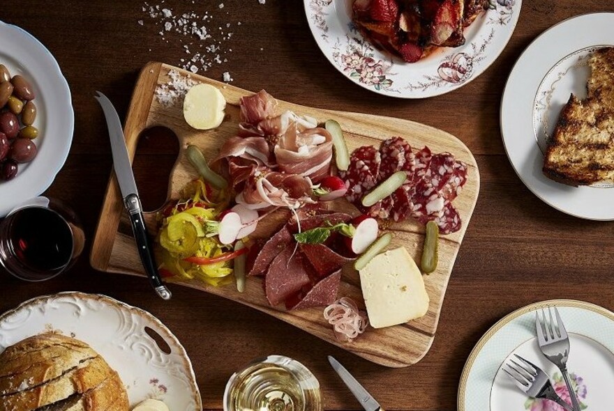 Overhead display of an antipasto platter with cold cuts, pickles, cheese and bread.
