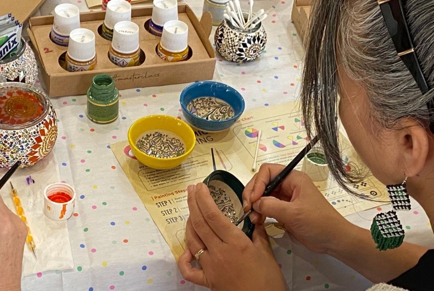 A person painting a bowl at a workshop table.