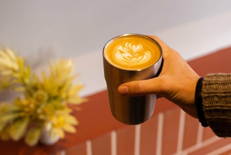 Hand holding an insulated keep cup filled with coffee.