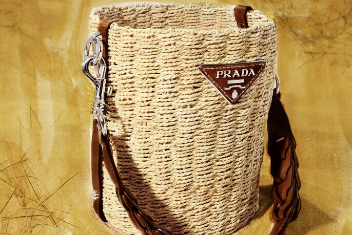 Beige woven raffia and leather handbag with plaited handle and Prada logo.