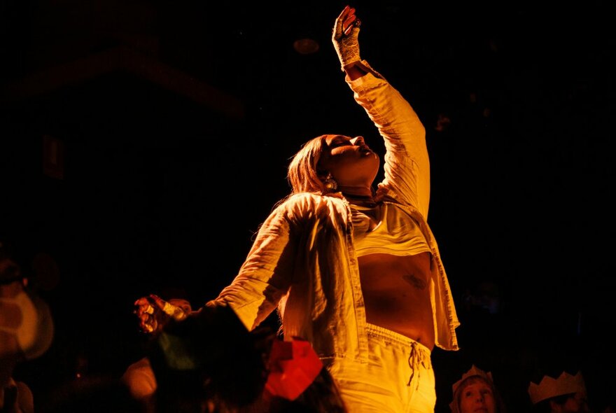 A cabaret dancer on stage with her arm in the air, wearing an open shirt.