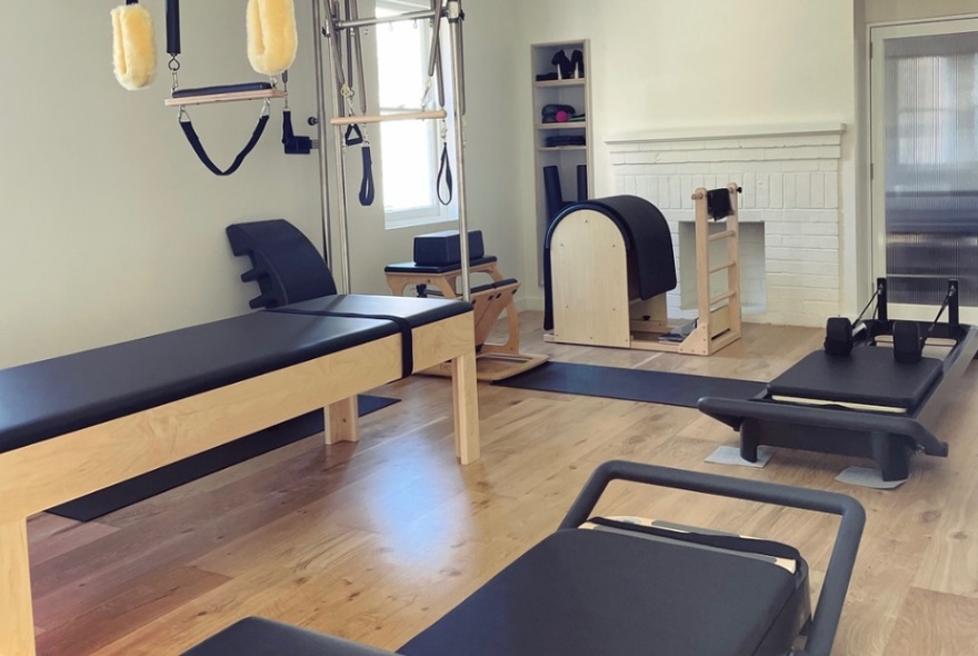 Pilates reformer machines and other equipment in a studio space with white walls and wooden floors.