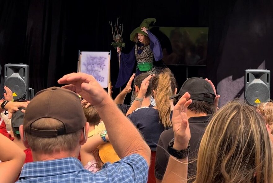 Audience members watching a wizard actor performing on stage.