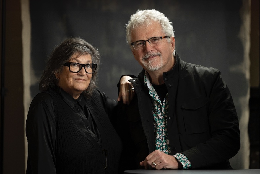 Writers Ian J McNiven and Lynette Russell standing together and smiling in a dark environment. 
