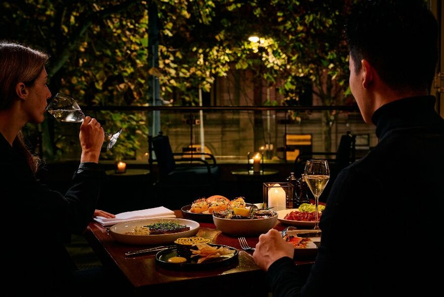 Two people at outdoor table, at night, seen from side/back.