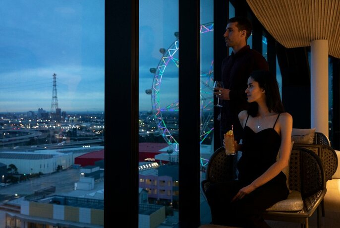 Couple looking out floor-to-ceiling windows at dusk, with Melbourne Star in view.
