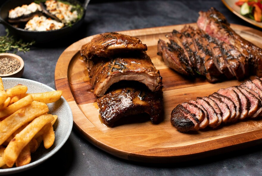 A wooden board with sliced steak and a bowl of chips.