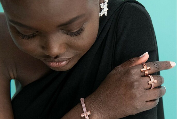 Model wearing rose gold cross-shaped rings and bracelet, with diamond earrings.