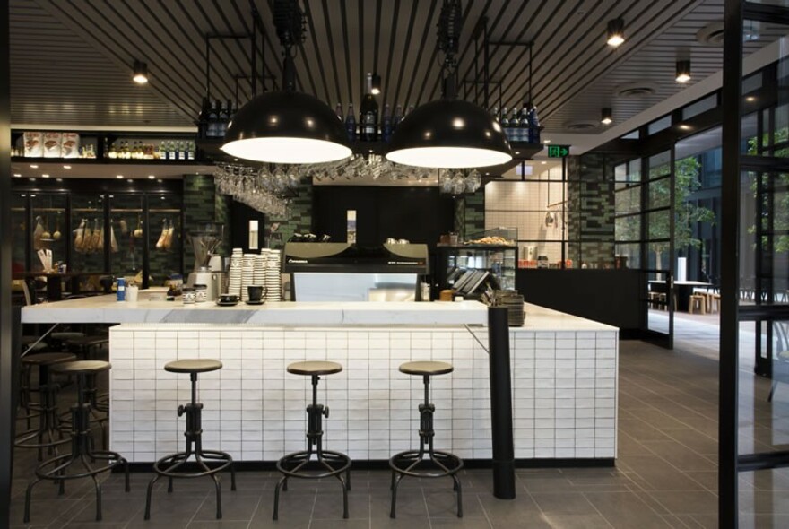 Interior of Mr Collins: white tiled bar with industrial-looking stools and large overhead lights.