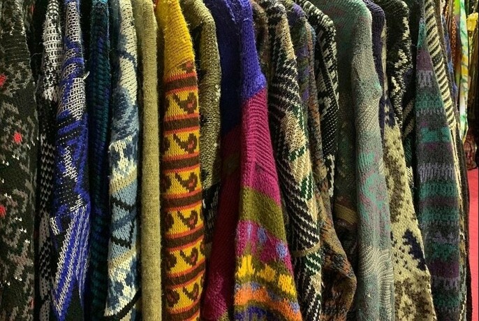 Rack of brightly coloured vintage jumpers lined up in a row.