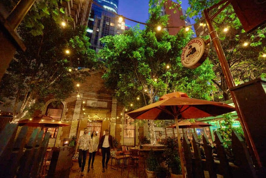 A group of three friends walking beneath fairy lights in a courtyard