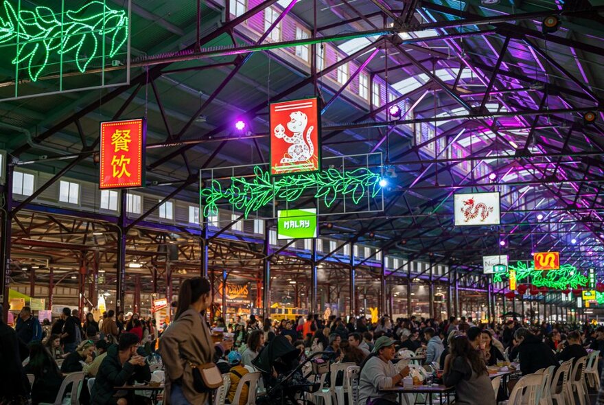Queen Vic market hall transformed into a night market with tables and chairs, overhead banners and neon.