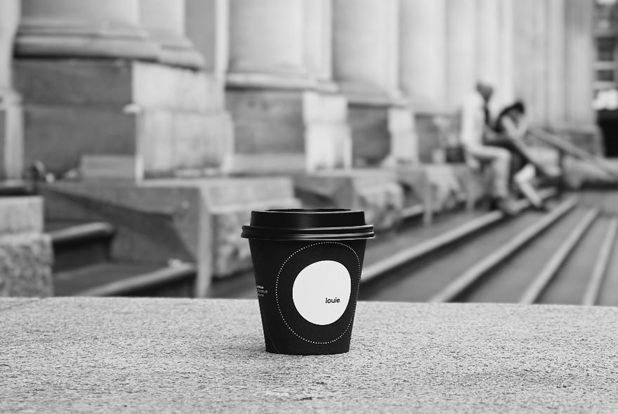 A black and white image of a black takeaway coffee cup with the steps of Melbourne's GPO in the background. 