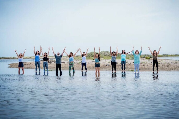 Row of people with hands above their heads and standing in shallow water.