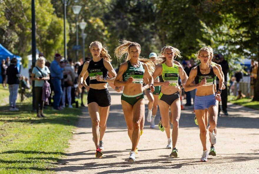Serious athletes running on an outdoor track, grass and trees surrounding them and spectators on the sidelines watching. 