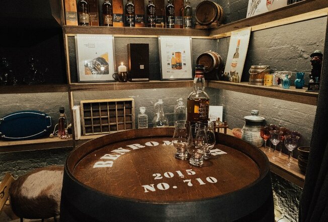 A bottle of whiskey on top of a barrel in a bar's barrel room.