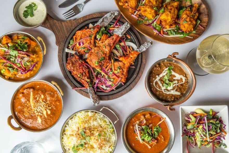 Table with assortment of dishes in copper pans including tandoori chicken and rice.