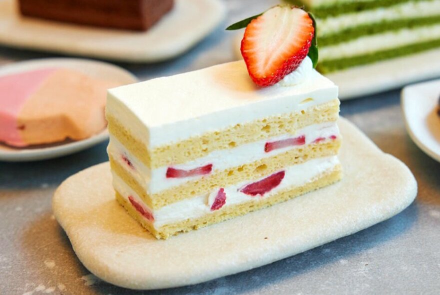 A rectangular slice of multi-layer sponge cake with cream and strawberries