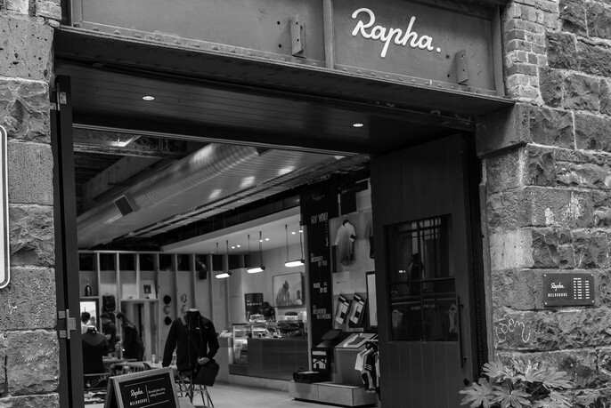 Exterior of the Rapha shopfront showing bluestone wall, signage and a glimpse of the inside.