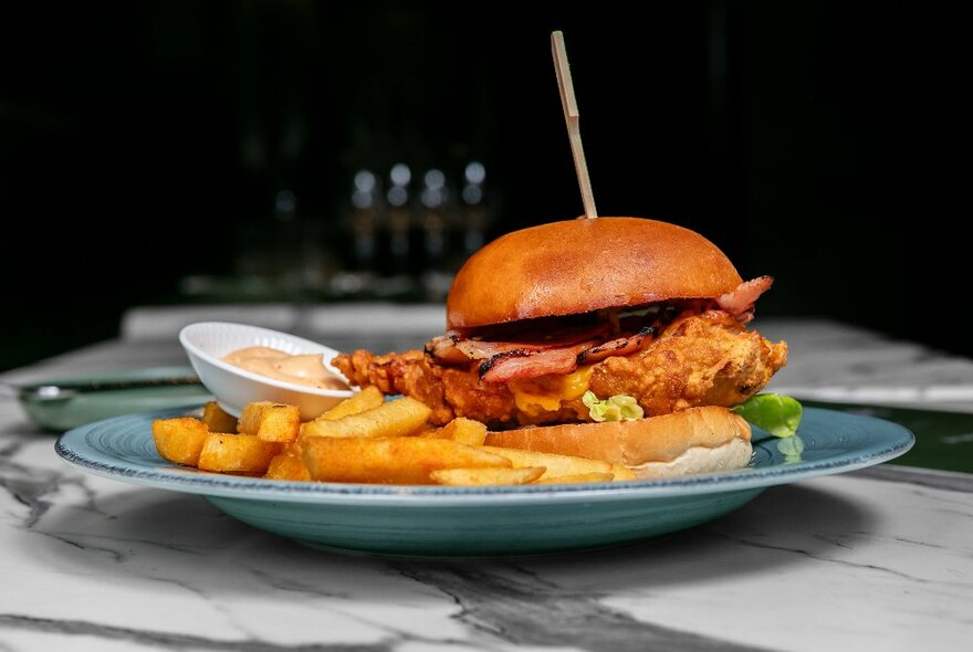 Side view of a stacked burger, with a side of fires, on a dinner plate on a restaurant table.