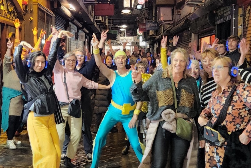 Group dancing in a Melbourne laneway, led by a man in a bright green and yellow shiny outfit.