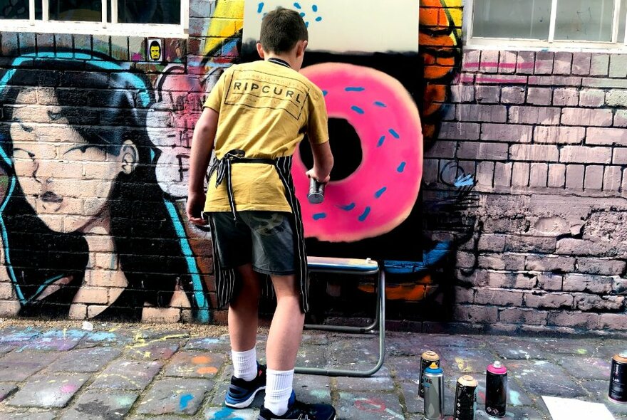 Child working on spray painted canvas, from behind.