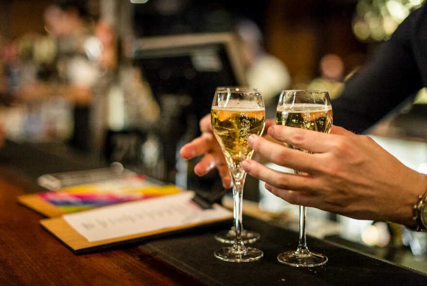 Hands carrying three glasses of bubbles from a wooden bar.